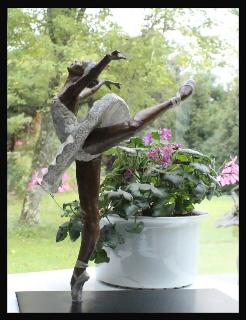 A statue of a ballerina in front of a flower pot.