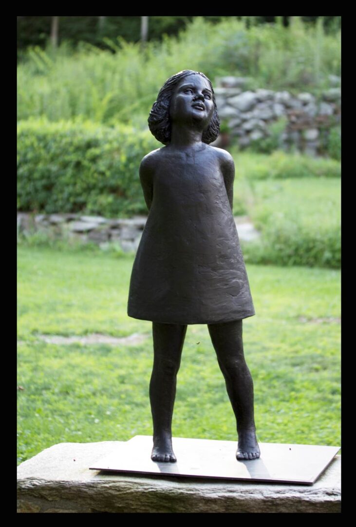 A statue of a little girl in the grass.
